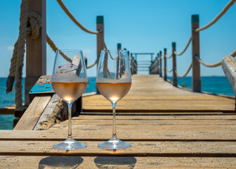 Glasses of cold rose wine from Provence served outdoor on wooden yacht pier with view on blue water...