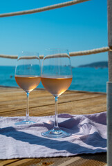 Glasses of cold rose wine from Provence served outdoor on wooden yacht pier with view on blue water and white sandy beach Plage de Pampelonne near Saint-Tropez, France