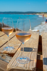 Glasses of cold rose wine from Provence served outdoor on wooden yacht pier with view on blue water and white sandy beach Plage de Pampelonne near Saint-Tropez, France