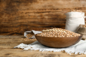 Bowl of wheat grains and spikes on wooden table. Space for text