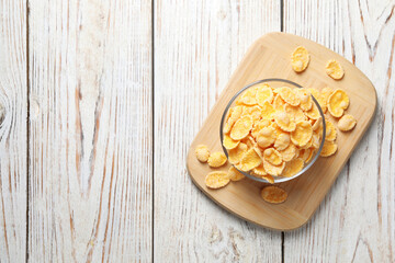 Fototapeta na wymiar Glass bowl of tasty crispy corn flakes on white wooden table, top view. Space for text