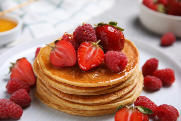 Tasty pancakes with fresh berries and honey on plate, closeup
