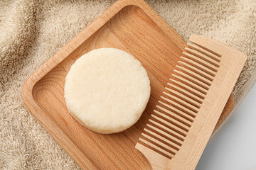 Solid shampoo bar, wooden comb and towel on light table, flat lay