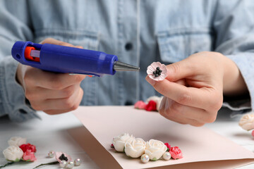 Woman using hot glue gun to make craft at white table, closeup