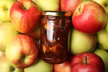 Delicious apple jam in jar on fresh fruits, top view