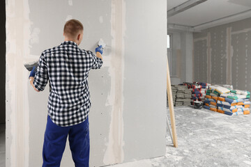 Man plastering wall with putty knife indoors, back view and space for text. Home renovation