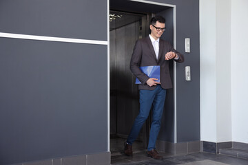 Young businessman walking out of modern elevator