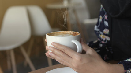 girl drinking and enjoying coffee during working in cafe. Close-up photo of Asian woman smelling and drinking hot coffee with good vibes in a cafe.