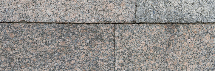 Wall of granite blocks. Rough surface of rock with a grainy pattern. Stone wall in classic style. Wide panoramic texture for background and design.