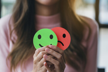 Woman Hands holding sad face hiding or behind happy smiley face, bipolar and depression, mental health concept, personality, mood change, therapy healing split concept. - obrazy, fototapety, plakaty