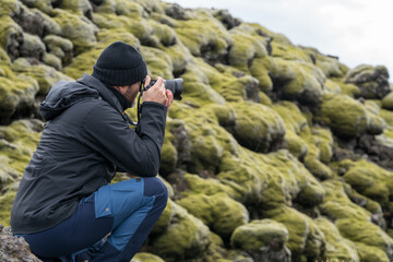 portrait of young adventurous man photographing mossy volcanic lava structures