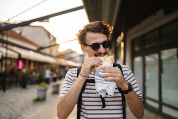 One man young adult modern caucasian male in the city in sunny day walk and eat sandwich fast food...