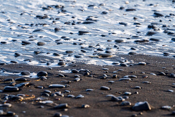Foam from waves breaking on small black volcanic rocks on an island beach during autumn winter
