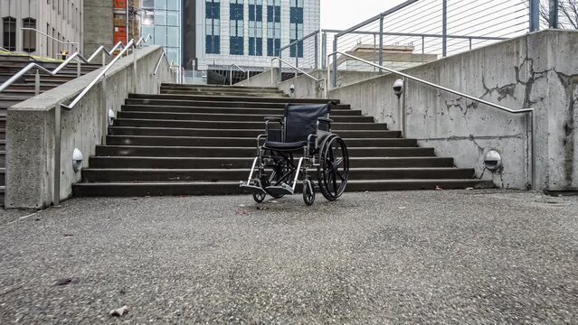
Approaching an empty wheelchair sitting at the base of cement steps in an empty outdoor urban courtyard.