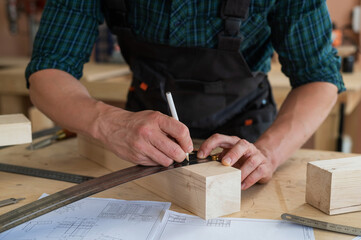 A carpenter measures wooden planks and makes marks with a pencil in a workshop.