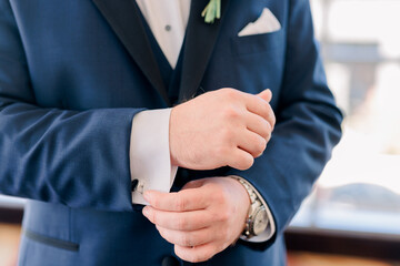 Groom wearing a blue suit holding his cufflink