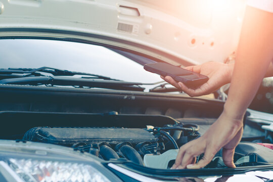 Woman Using Mobile Phone While Looking At Broken Down Car On Road.