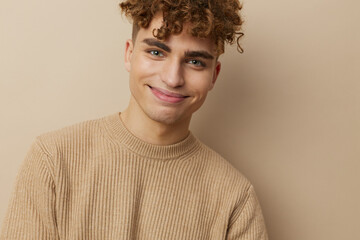 Fototapeta premium close horizontal portrait of a handsome, charming man with curly hair standing in a beige sweater on a beige background