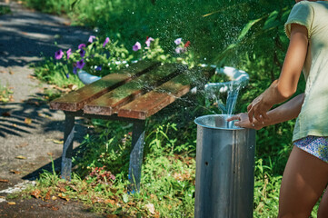 In summer, a girl plays with a drinking fountain in the park. Back view. A cloud of water splashes...