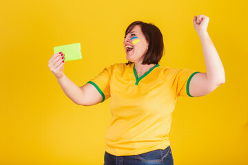 red-haired woman, Brazilian soccer fan. watching the football match on mobile. Football match...
