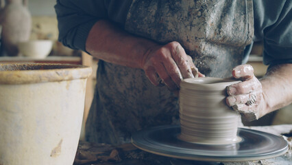 Close-up shot of half-finished ceramic vase spinning on potters's wheel and male hands molding clay...
