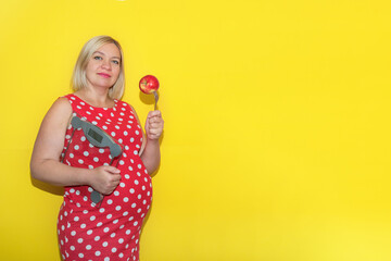 pregnant woman in a red polka dot dress with scales and an apple on a fork on a yellow background...
