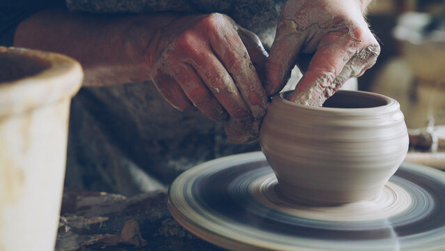 Work in pottery workshop: clay ware on throwing wheel, master ceramist molding clay using professional tools. Creating ceramic utensils and traditional occupation concept.
