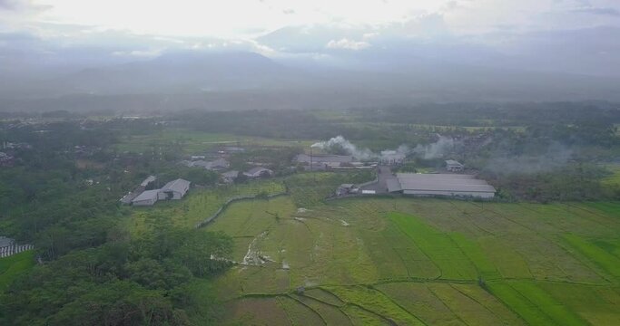 Aerial footage of Factory with a chimney that emits smoke to sky in scenic area of Indonesia - Environmental Pollution of nature