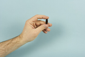 A man's hand holds a black capsule. The concept is vitamins for men.