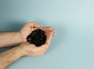 The men's palms are filled with black capsules on a blue background. The concept is vitamins for...