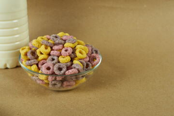 Transparent cornflake ring breakfast plate with a bottle of milk on a brown background. The concept is a quick and ready breakfast.