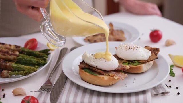 making egg benedict - woman pouring hollandaise sauce onto poached egg