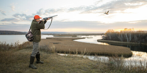  waterfowl hunter shooting into sky during duck hunting at sunrise. hunting banner - obrazy, fototapety, plakaty