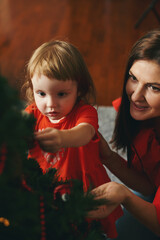 Caucasian girl and mom in red clothes decorating fir tree on Christmas holidays