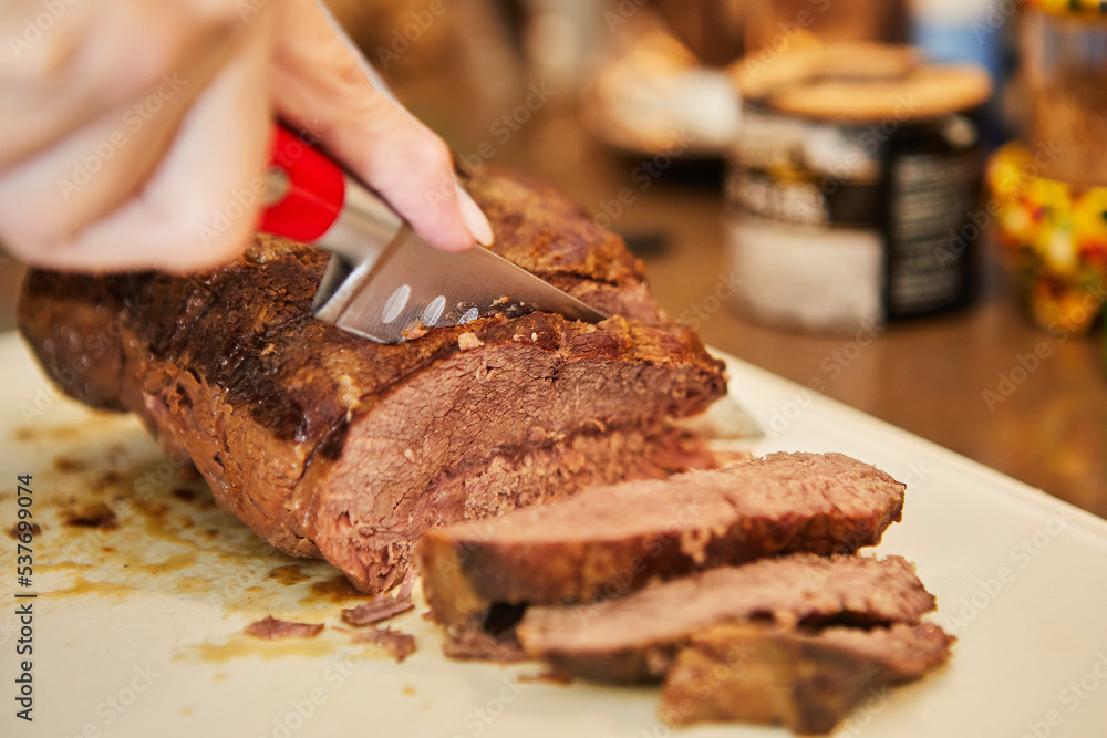 Sticker Chef cuts piece of beef fried with onions in wine sauce into slices for serving. French gourmet cuisine