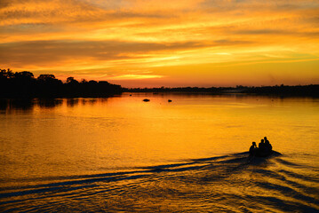 The silhouette of a small motorized canoe against a golden dusk on the Guaporé - Itenez river,...