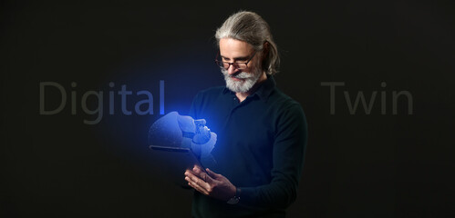 Senior businessman with tablet computer and his digital projection on dark background. Concept of...