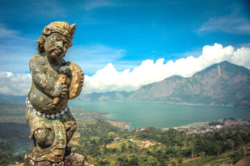 Fototapeta na wymiar A small statue on a hill with a lake and mountains in the background in bali