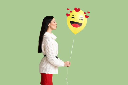 Beautiful young woman holding balloon with drawn smile on green background