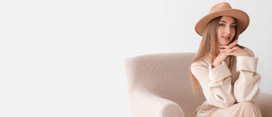 Beautiful fashionable young woman in elegant clothes sitting in armchair on light background with space for text