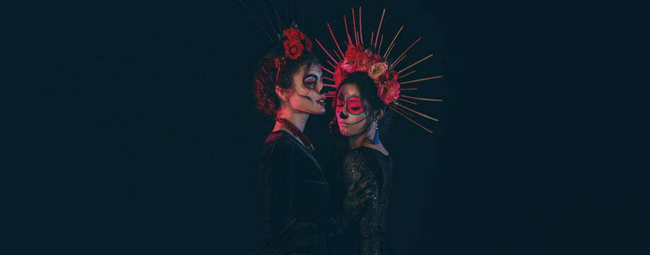 Women with painted skulls on faces against dark background. Celebration of Mexico's Day of the Dead (El Dia de Muertos)