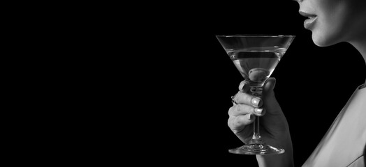 Black and white photo of beautiful young woman drinking martini on dark background with space for text, closeup