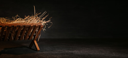 Manger with hay on dark background with space for text. Concept of Christmas story