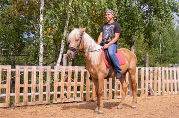 Outside on a beautiful warm day, a young man is riding a horse.