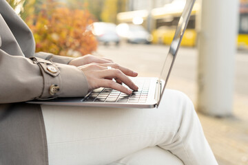 Female typing on laptop keyboard outdoors. Woman using laptop in the city
