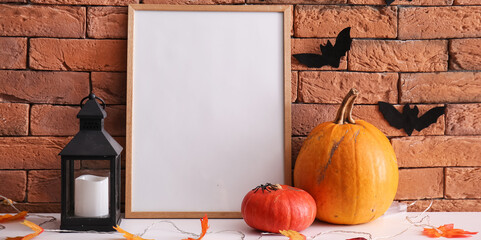 Blank photo frame with Halloween pumpkins, lantern and autumn leaves on table near brick wall