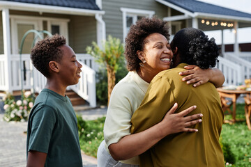 Waist up portrait of African American family embracing while welcoming guests for Summer party...