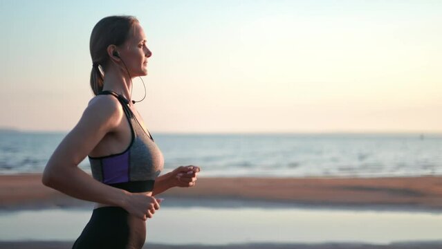 Happy female jogger runner outdoor cardio fitness training at sunset sunrise coast beach slow motion