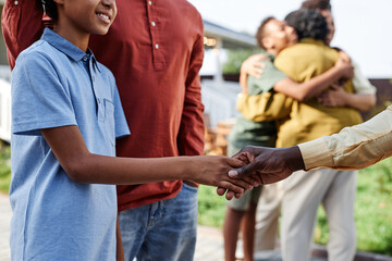 Side view closeup of young African American boy shaking hands with family member during Summer...