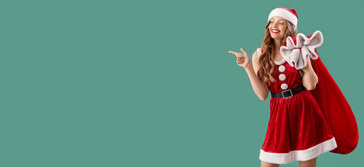 Pretty young woman in Santa costume pointing at something on green background with space for text